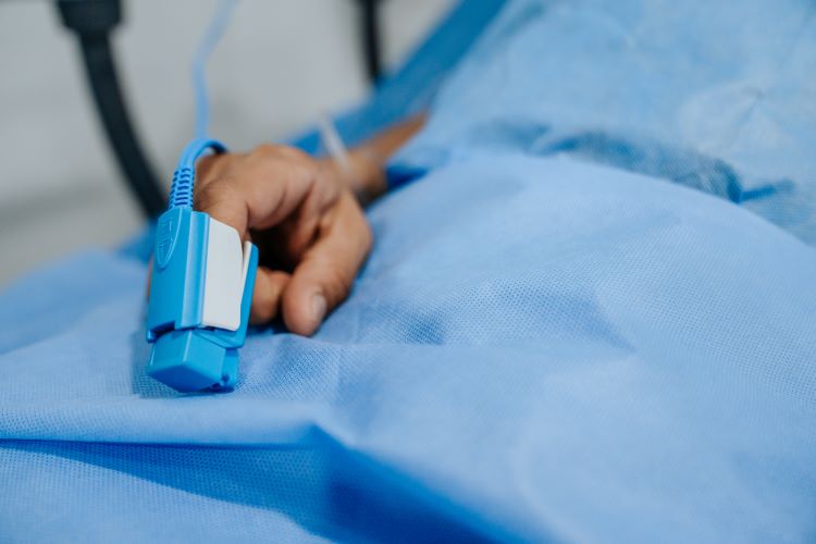 hand with oxygen monitor on blue blanket; photo by Cesar Badilla Miranda